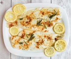 fish with lemons and herbs on a white plate next to some slices of lemon