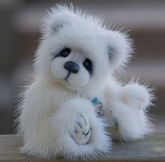 a small white teddy bear sitting on top of a wooden table with its paws up