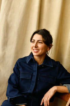 a woman sitting on top of a wooden chair next to a curtain in front of a window