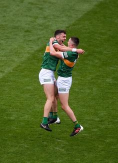 two men in green and white uniforms are hugging each other on the field with their arms around one another