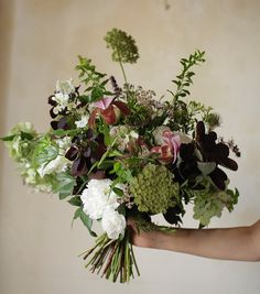 a woman holding a bouquet of flowers in her hand with greenery on the side