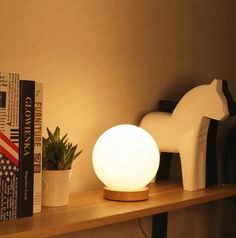 a white light sitting on top of a wooden shelf next to a plant and books