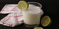 a glass filled with milk and limes on top of a table next to a towel