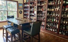 a room filled with lots of bottles and chairs next to a wooden table in front of a window