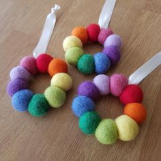 four different colored felt balls are arranged in a circle on a wooden surface with white ribbon