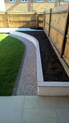 a garden area with grass and gravel in the middle, next to a wooden fence