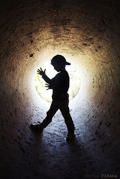 a person walking through a dark tunnel with their hands in the air while wearing a hat