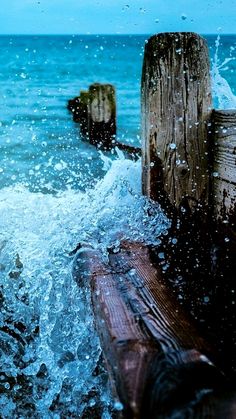 the water is splashing over the wooden bench by the ocean's shore line