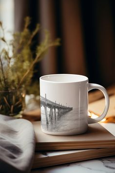 a white coffee mug sitting on top of a book next to a vase with flowers