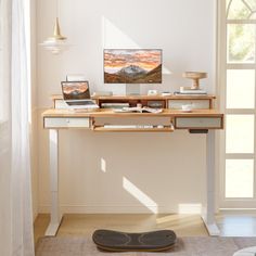 a laptop computer sitting on top of a wooden desk next to a skateboard in front of a window