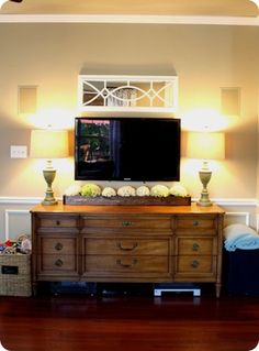 a flat screen tv sitting on top of a dresser in a living room next to two lamps