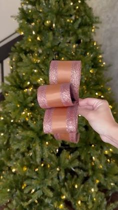 someone is holding two rolls of ribbon in front of a christmas tree