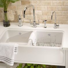 a white sink sitting under a window next to a potted plant and two glasses