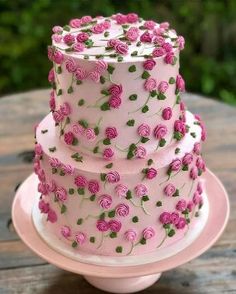 a three tiered cake with pink flowers on it sitting on top of a wooden table