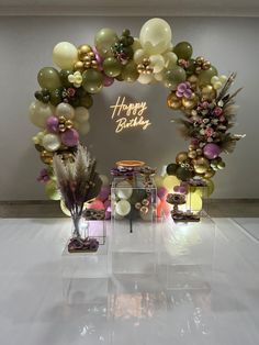 a happy birthday arch with balloons and flowers on display in front of a white wall