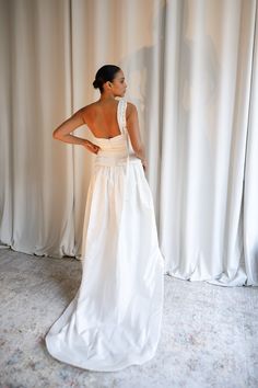 a woman standing in front of a curtain wearing a white wedding dress with an open back