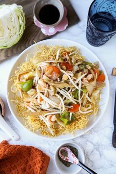 a white plate topped with noodles and veggies next to a cup of coffee