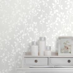 a white dresser topped with lots of drawers next to a wallpaper covered in leaves