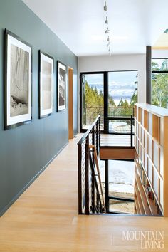 a long hallway with pictures on the wall and wooden stairs leading up to an open door