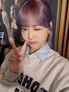 a young woman with purple hair making the peace sign while sitting in front of a poster