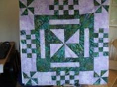 a green and white quilt hanging from a wall next to a computer desk with a keyboard on it