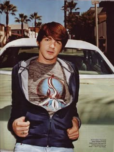 a young man standing in front of a car with his hands on his hips and looking at the camera