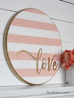 a pink and white painted circle with the word love on it next to some flowers