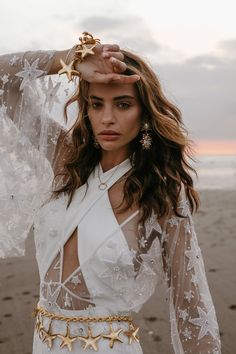 a woman standing on top of a beach next to the ocean wearing a white dress