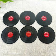 six black records with red labels on them sitting on a white cloth covered tablecloth