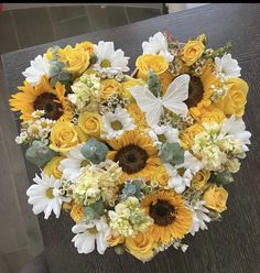 a bouquet of sunflowers and daisies in the shape of a heart on a table