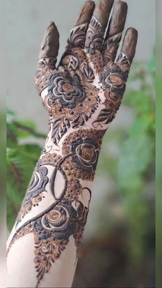 a woman's hand with henna on it and some plants in the background