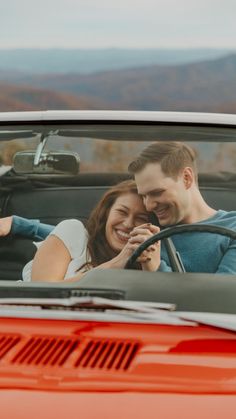 a man and woman sitting in the driver's seat of a red car