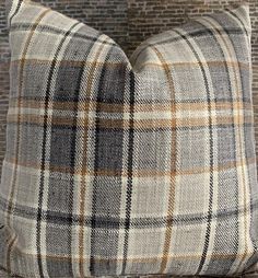 a plaid pillow sitting on top of a wooden table next to a brick wall and lamp