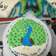 there is a birthday cake decorated with a peacock on the front and back sides, along with a slice missing from it