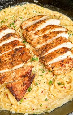 two pieces of chicken on top of pasta in a skillet