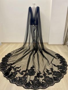 a black veil with flowers on it sitting on top of a wooden floor in front of a white wall