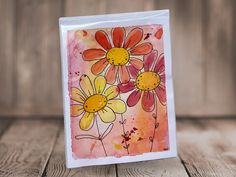 a card with watercolor flowers on it sitting on a table next to a wooden wall