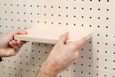 two hands are holding a piece of wood on a peg board that has holes in it