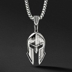 a silver Spartan pendant in the shape of a helmet with one side battle worn Warrior Style Engraved Pendant Jewelry, Engraved Warrior Style Pendant Jewelry, Warrior Style Engraved Sterling Silver Jewelry, Silver Engraved Warrior Necklace, Silver Tarnish Resistant Amulet Necklace, Silver Tarnish-resistant Amulet Necklace, Silver Warrior Style Necklace For Gift, Mens Silver Pendants, Pendants For Men