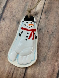 a ceramic snowman ornament hanging from a rope on a wooden table with wood planks