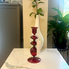 a red vase sitting on top of a white counter next to a potted plant