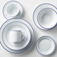 four white plates with blue trim around them and two cups on the top one has a saucer in the middle