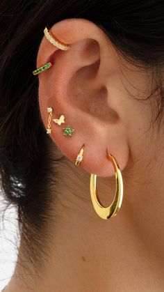 a close up of a person wearing gold ear cuffs with green and white stones on them