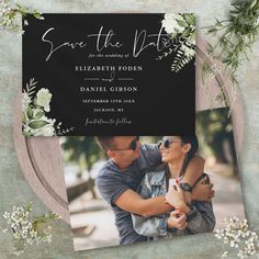 the save the date photo card is shown with flowers and greenery on black paper