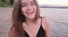 a woman standing on the beach with her hair blowing in the wind and smiling at the camera