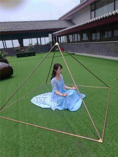 a woman sitting on top of a grass covered field next to a large triangular structure