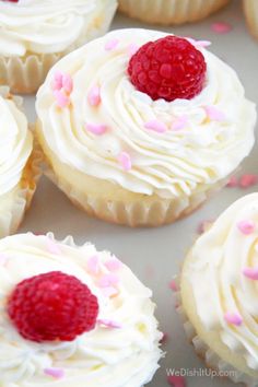 some cupcakes with white frosting and raspberries on top are ready to be eaten