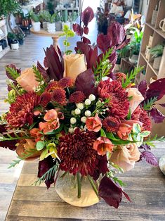 a vase filled with red and orange flowers on top of a wooden table in a store