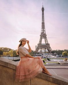 a woman in a pink dress and hat sitting on a ledge near the eiffel tower