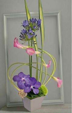 an arrangement of flowers in a vase on a table next to a framed photo with a gray frame